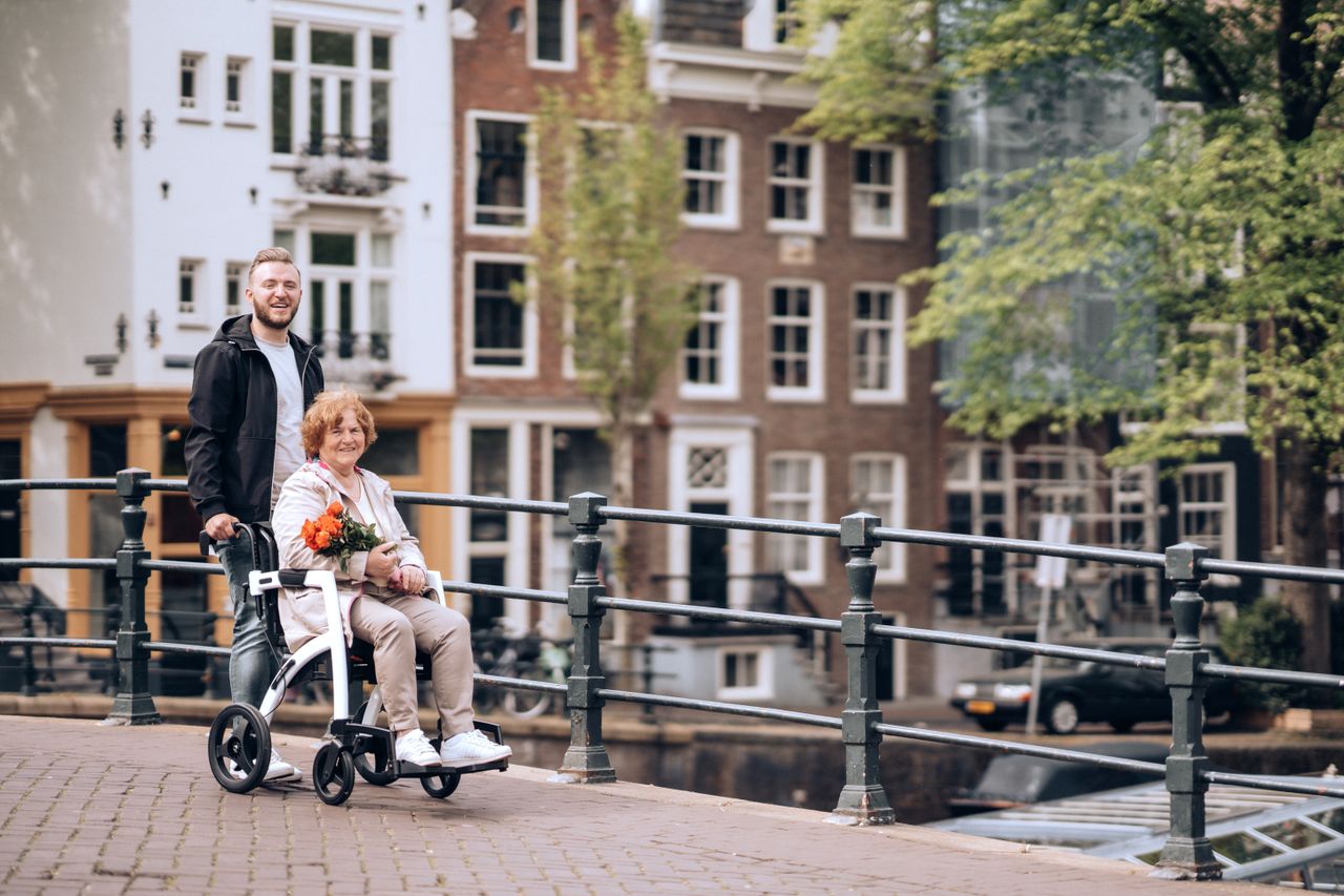 A senior woman in a wheelchair with flowers enjoys a stroll along Amsterdams iconic canals.